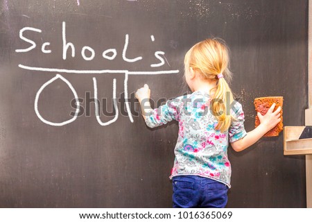 Cute little girl writing Schools's out on chalkboard in a classroom