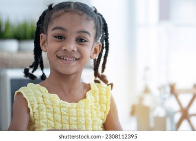 Cute little girl in yellow dress and braided hair smiling in her kitchen - Powered by Shutterstock