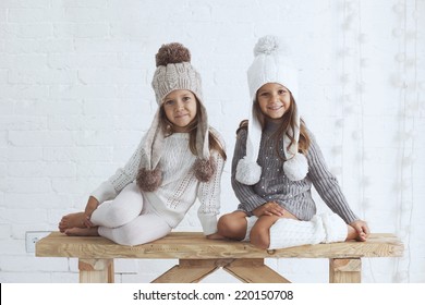 Cute little girls of 5 years old wearing knitted trendy winter clothes posing over white brick wall