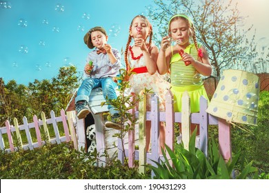 Cute little girls with boy are blowing a soap bubble