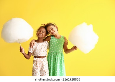 Cute little girls with cotton candy on yellow background