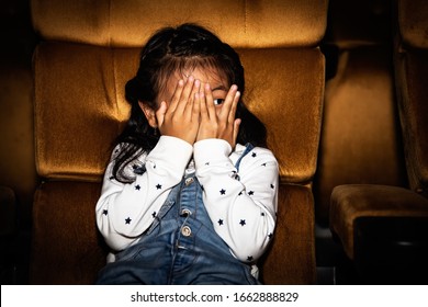 Cute little girls sit and watch fun movies in a thrilling cinema with horror and thrilling, using hands to cover their faces, leaving only the eyes to want to thrill. - Shutterstock ID 1662888829