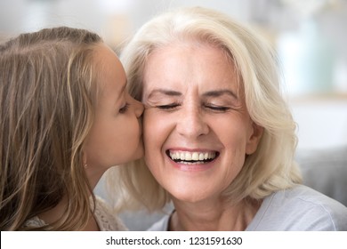 Cute Little Granddaughter Kissing Smiling Old Grandmother On Cheek, Preschool Grandchild Girl Congratulates Happy Grandma With Mothers Day Birthday Expressing Love Warm Relations With Laughing Granny