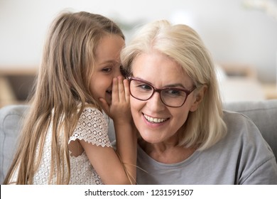 Cute little granddaughter whispering in ear telling secret to understanding smiling grandma, kid girl secretly talking to granny having fun gossiping, trust in grandmother and grandchild relations