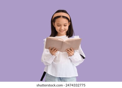 Cute little happy Asian girl with backpack reading book on purple background. End of school year - Powered by Shutterstock