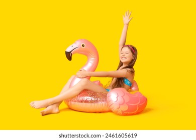 Cute little happy girl in swimsuit with inflatable ring and goggles sitting on yellow background - Powered by Shutterstock