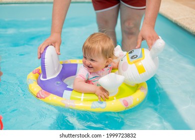 A Cute Little Happy Smiling Kid Baby Girl Is Swimming In The Swimming Pool Under Supervision Of Adults. Child Safety And Vacation Concept