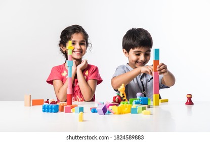 Cute Little Indian Asian Kids Playing With Colourful Plastic Toys Or Blocks While Sitting At Table Or Isolated Over White Background