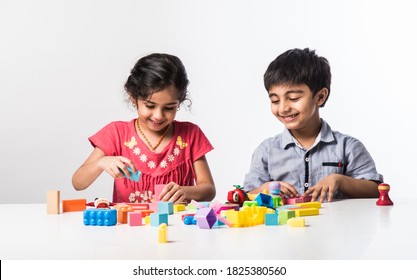 Cute Little Indian Asian Kids Playing With Colourful Plastic Toys Or Blocks While Sitting At Table Or Isolated Over White Background