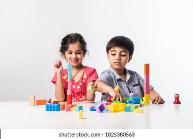 Cute Little Indian Asian Kids Playing With Colourful Plastic Toys Or Blocks While Sitting At Table Or Isolated Over White Background