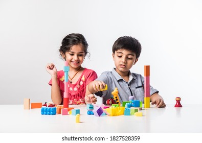 Cute Little Indian Asian Kids Playing With Colourful Plastic Toys Or Blocks While Sitting At Table Or Isolated Over White Background