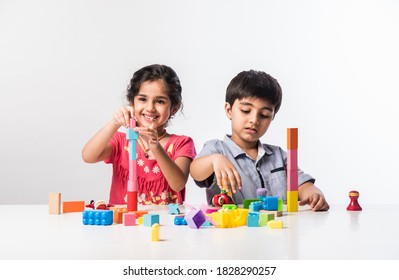 Cute Little Indian Asian Kids Playing With Colourful Plastic Toys Or Blocks While Sitting At Table Or Isolated Over White Background