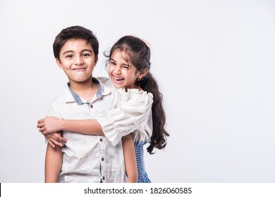 Cute little Indian asian siblings standing and embracing each other in white clothes while standing againstwhite background.
