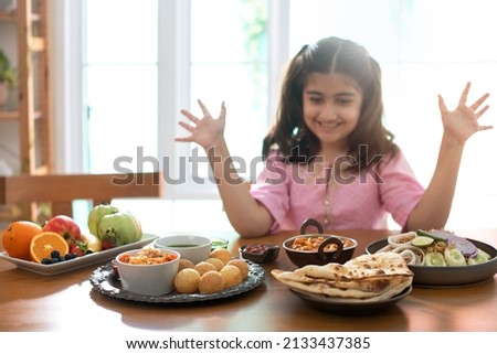 Cute little Indian girl is enjoying her favorite Indian food, surprised girl raised hands 