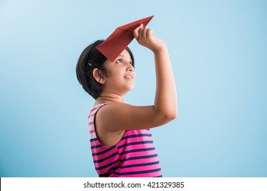 Cute Little Indian Girl Flying A Handmade Paper Aeroplane, Isolated Over Blue Or White Background