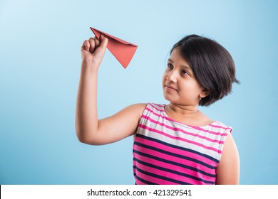 Cute Little Indian Girl Flying A Handmade Paper Aeroplane, Isolated Over Blue Or White Background