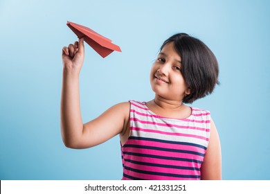 Cute Little Indian Girl Flying A Handmade Paper Aeroplane, Isolated Over Blue Or White Background