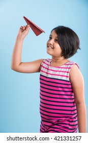 Cute Little Indian Girl Flying A Handmade Paper Aeroplane, Isolated Over Blue Or White Background