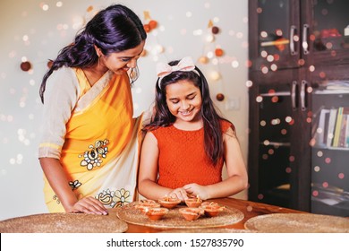 Cute little Indian girl lighting diyas for Diwali together with her mother at home
