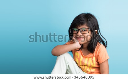 Cute little Indian girl with spectacles smiling and posing for photoshoot, against sky blue background