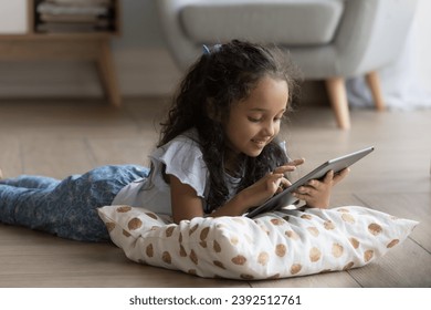 Cute little Indian girl using digital tablet, play video games on-line, spend time on internet alone at home. Generation Alpha and modern wireless tech, parental control software, apps usage concept - Powered by Shutterstock