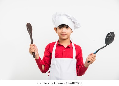 Cute Little Indian Kid/boy Dressed As A Chef And Holding Cooking Utensils, Standing Isolated Over White Background