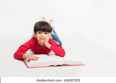 Cute little Indian/asian boy reading book while sitting or lying over white background