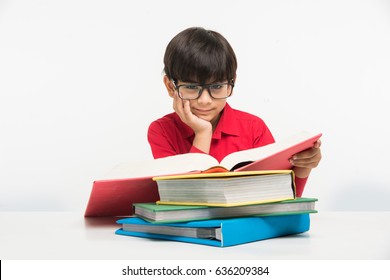 Cute little Indian/Asian boy reading book over study table, isolated over white background