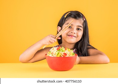 Cute Little Indian/Asian Girl Child Eating Yummy Chinese Noodles With Fork Or Chopsticks, Isolated Over Colourful Background