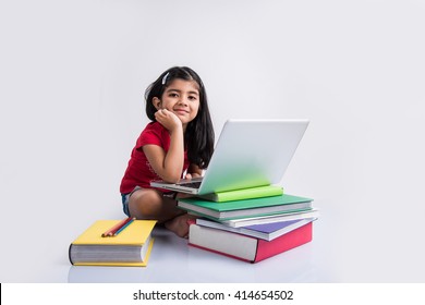 Cute Little Indian/Asian Girl Child Studying On Laptop Or Reading Books While Lying On The Floor, Isolated Over White Background