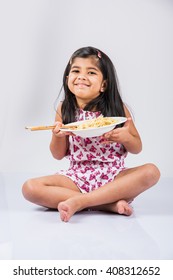 Cute Little Indian/Asian Girl Eating Yummy Chinese Noodles With Fork Or Chopsticks, Isolated Over Colourful Background