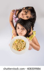 Cute Little Indian/Asian Girls Eating Yummy Chinese Noodles With Fork Or Chopsticks, Isolated Over Colourful Background