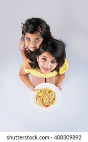 Cute Little Indian/Asian Girls Eating Yummy Chinese Noodles With Fork Or Chopsticks, Isolated Over Colourful Background