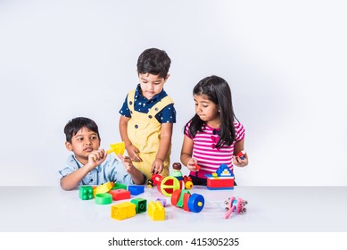 Cute little Indian/asian kids playing with toys or blocks and having fun while sitting at table or isolated over white background
