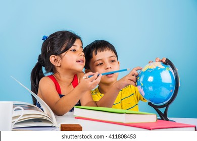 Cute little Indian/Asian kids studying on study table with pile of books, educational globe, isolated over light blue colour
