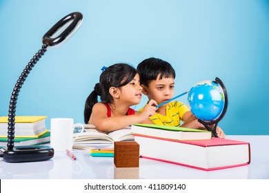 Cute Little Indian/Asian Kids Studying On Study Table With Pile Of Books, Educational Globe, Isolated Over Light Blue Colour