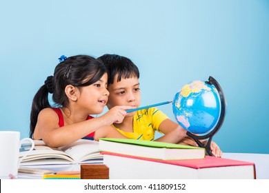 Cute little Indian/Asian kids studying on study table with pile of books, educational globe, isolated over light blue colour - Powered by Shutterstock