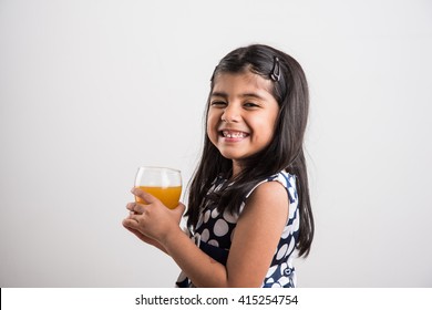 Cute Little Indian/Asian Playful Girl Drinking Fresh Mango/orange Juice / Cold Drink In A Glass, Isolated Over  White Background