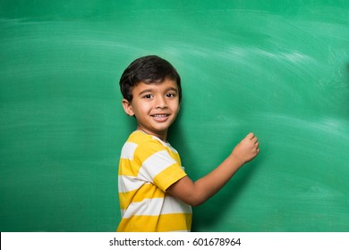 cute little indian/asian school boy writing over green chalkboard background with copy space - Powered by Shutterstock