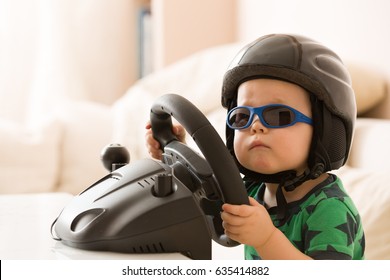 Cute little kid boy in a helmet playing with Computer steering wheel. Future driver. Getting ready for professional driving. Child driving a car. Funny toddler boy indoors. Boy and a car.