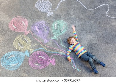 Cute little kid boy playing   flying and colorful balloons picture drawing and chalk  Creative leisure for children outdoors in summer  celebrating birthday