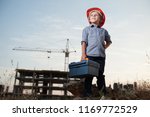 cute little kid in builder helmet with toolbox in hand on standing construction site