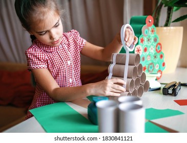 Cute little kid making handmade advent calendar with toilet paper rolls at home. Glue, colored paper, cut punch to hide sweets and candies in rolls. Seasonal activity for kids, family winter holidays