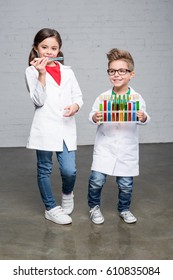 Cute Little Kids In Lab Coats Holding Test Tubes With Colorful Chemical Samples