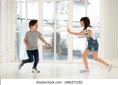 Cute Little Kids Siblings Playing Tag And Touch Game At Home, Two Excited Happy Small Children Boy And Girl Running Laughing Catching Each Other In Funny Activity Inside Modern Living Room Indoor