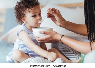 Cute Little Mixed Race Baby Girl Sitting On Bed And Eating.