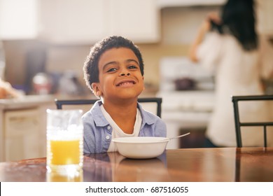 cute little mixed race boy smiling into camera with mother in background at breakfast