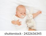 cute little newborn baby sleeping with a pacifier in his mouth under a blanket hugging a plush bunny, sweet healthy baby sleep in a white crib.