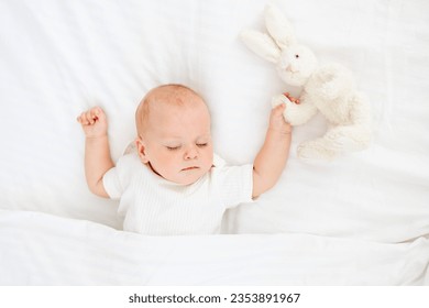 cute little newborn baby sleeping under a blanket hugging a plush bunny, sweet healthy baby sleep in a white crib, a place for text. - Powered by Shutterstock