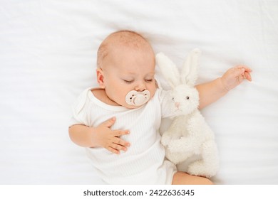 cute little newborn baby sleeping with a pacifier in his mouth under a blanket hugging a plush bunny, sweet healthy baby sleep in a white crib. - Powered by Shutterstock